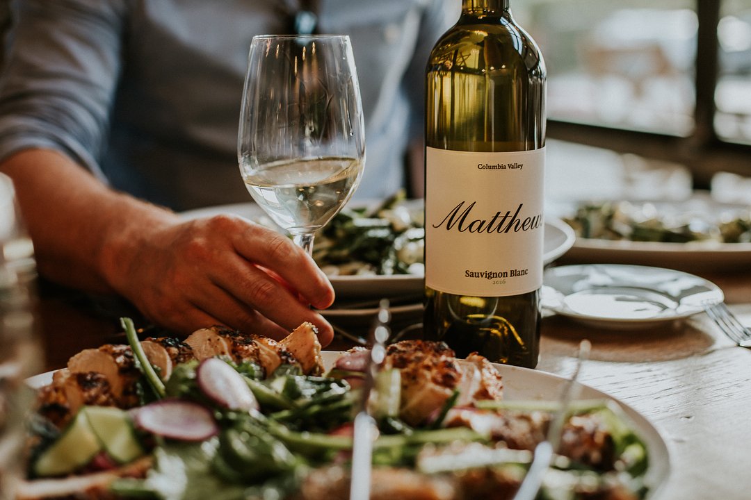 Person with glass of wine, and food, from Matthews Estate Winery near Bothell.